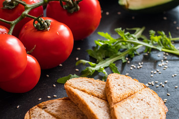 Tomatos and avocado on black table close up, colorful healthy food 