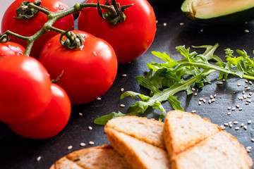 Tomatos and avocado on black table close up, colorful healthy food 