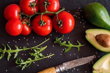 Tomatos and avocado on black table close up, colorful healthy food 