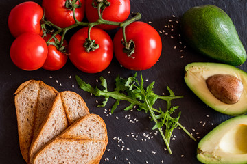 Tomatos and avocado on black table close up, colorful healthy food 