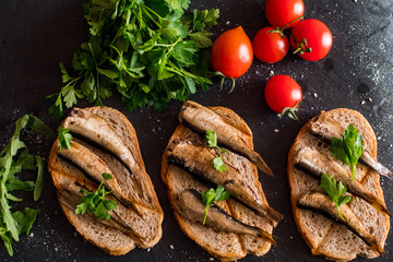 Close up of smoked sprats with tomatos on black table