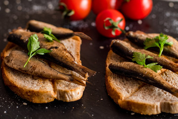 Close up of smoked sprats with tomatos on black table