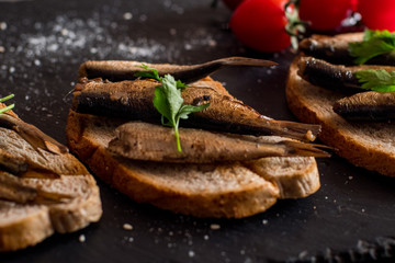 Close up of smoked sprats with tomatos on black table
