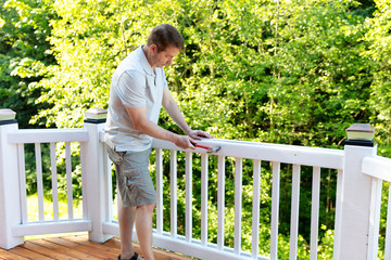 Mature man hammering nail into white railing of outdoor deck