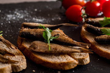 Close up of smoked sprats with tomatos on black table
