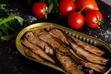 Close up of smoked sprats with tomatos on black table