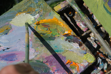 artist brush mix color oil painting on palette is holding in his hand closeup