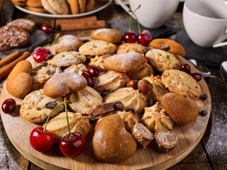 Oatmeal cookies and sand chocolate cake with cherry berry on cutting board on wooden table in rustic style. Cups and dessert spoons. Easily digestible and quickly digestible substances.