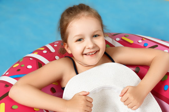 Cute little girl in a swimsuit is lying on a donut inflatable circle. The child is holding a white hat. Closeup portrait. Blue background.