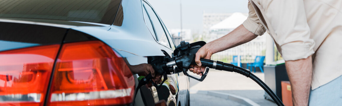 Panoramic shot of man holding fuel pump and refueling black car
