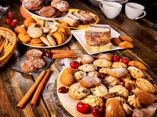 Oatmeal cookies and sand chocolate cake with cherry berry and crispy wafer rolls with cream on cutting board on wooden table in rustic style. Limitations for diabetics. Cherry in powdered sugar.