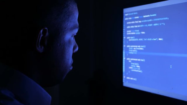 Portrait of african american man programmer coding network security software. Hacker typing code on computer screen in dark office at night