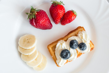 White plate with belgian waffles with strawberry, bananas and blueberries 