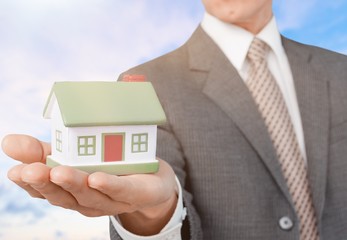 Building, mortgage, real estate and property concept - close up of hand holding house model