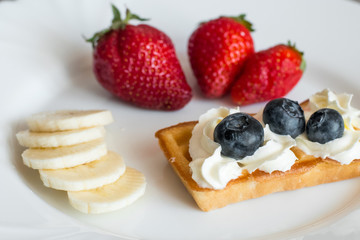 White plate with belgian waffles with strawberry, bananas and blueberries 