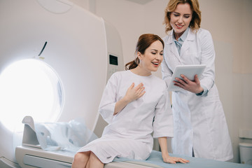 smiling radiologist showing x-ray diagnosis to happy patient sitting on ct scanner bed