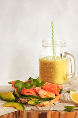 Homemade sliced salmon avocado sandwich snack and orange fresh fruit juice on the beeswax wraps paper in the kitchen.
