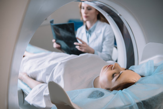 selective focus of radiologist holding x-ray diagnosis while patient lying on ct scanner bed during diagnostics