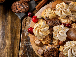 Oatmeal cookies and sand chocolate cake with cherry berry and crispy wafer rolls with cream on cutting board on wooden table in rustic style. Wide range of quality sweets.