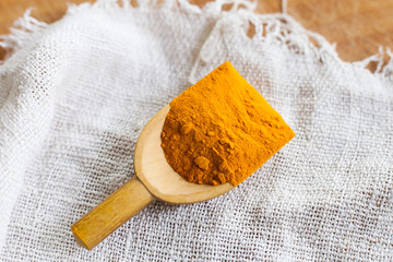 curcuma powder spice in wooden spoon on white linen background
