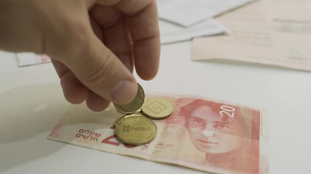 Small amount of Israeli money being put on table with bills