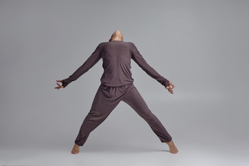 Photo of an athletic man ballet dancer dressed in a gray tracksuit, making a dance element against a gray background in studio.