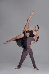 Two athletic modern ballet dancers are posing against a gray studio background.