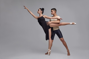Two athletic modern ballet dancers are posing against a gray studio background.