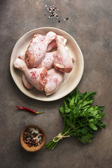 Raw chicken drumstick with spices and parsley on a dark rustic background. Top view, copy space.
