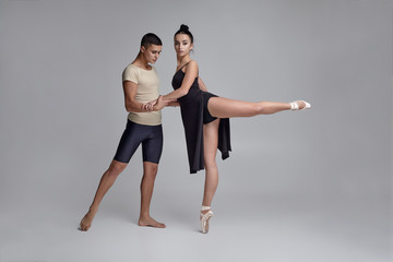 Two athletic modern ballet dancers are posing against a gray studio background.