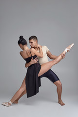 Two athletic modern ballet dancers are posing against a gray studio background.