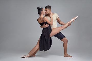Two athletic modern ballet dancers are posing against a gray studio background.