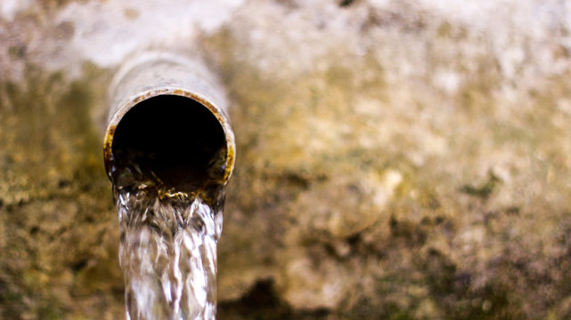 Water flow from old metal pipe. Blurred background. 