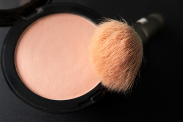 Peach blush and makeup brush on black background, close up