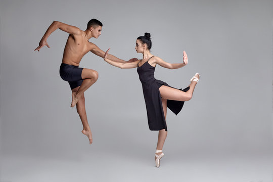 Two athletic modern ballet dancers are posing against a gray studio background.