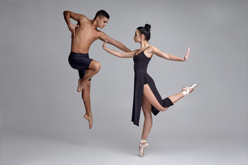 Two athletic modern ballet dancers are posing against a gray studio background.