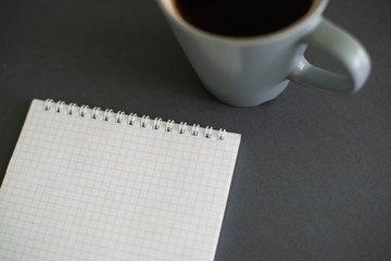 A cup of coffee on a gray background with a notepad  