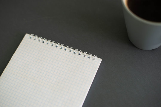 A cup of coffee on a gray background with a notepad  
