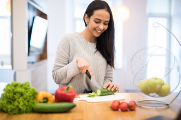 The young woman cuts vegetables in the kitchen with a knife and laptop on the table. Vegetable Salad. Diet. Dieting Concept. Healthy Lifestyle. Cooking At Home.