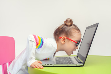 Excited beautiful little girl looking at laptop screen very closely