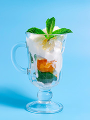 Summer dessert. ce cream with fruit and mint leaves in glass on a blue background.