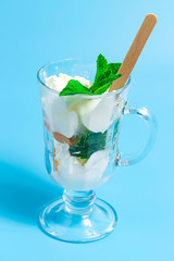 Summer dessert. ce cream with fruit and mint leaves in glass on a blue background.