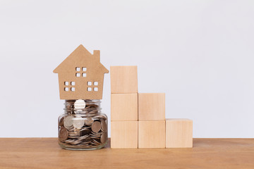 Money coins in glass jar and house model with Wooden cube stack a staircase on wooden table. Investment and saving concept