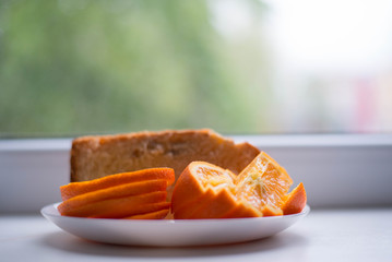 Oranges are sliced in a white plate. In the background there is also a piece of the pie