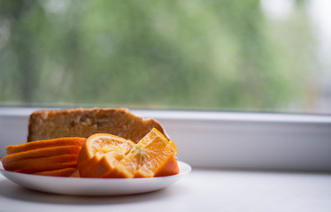 Oranges are sliced in a white plate. In the background there is also a piece of the pie