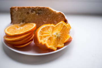 Oranges are sliced in a white plate. In the background there is also a piece of the pie