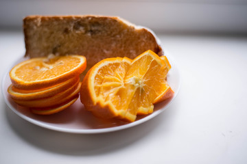 Fototapeta na wymiar Oranges are sliced in a white plate. In the background there is also a piece of the pie