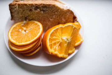 Oranges are sliced in a white plate. In the background there is also a piece of the pie