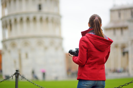 Young female tourist taking photos of the famous Leaning Tower of Pisa.