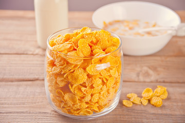 A bowl of dry corn flakes cereal on wooden background